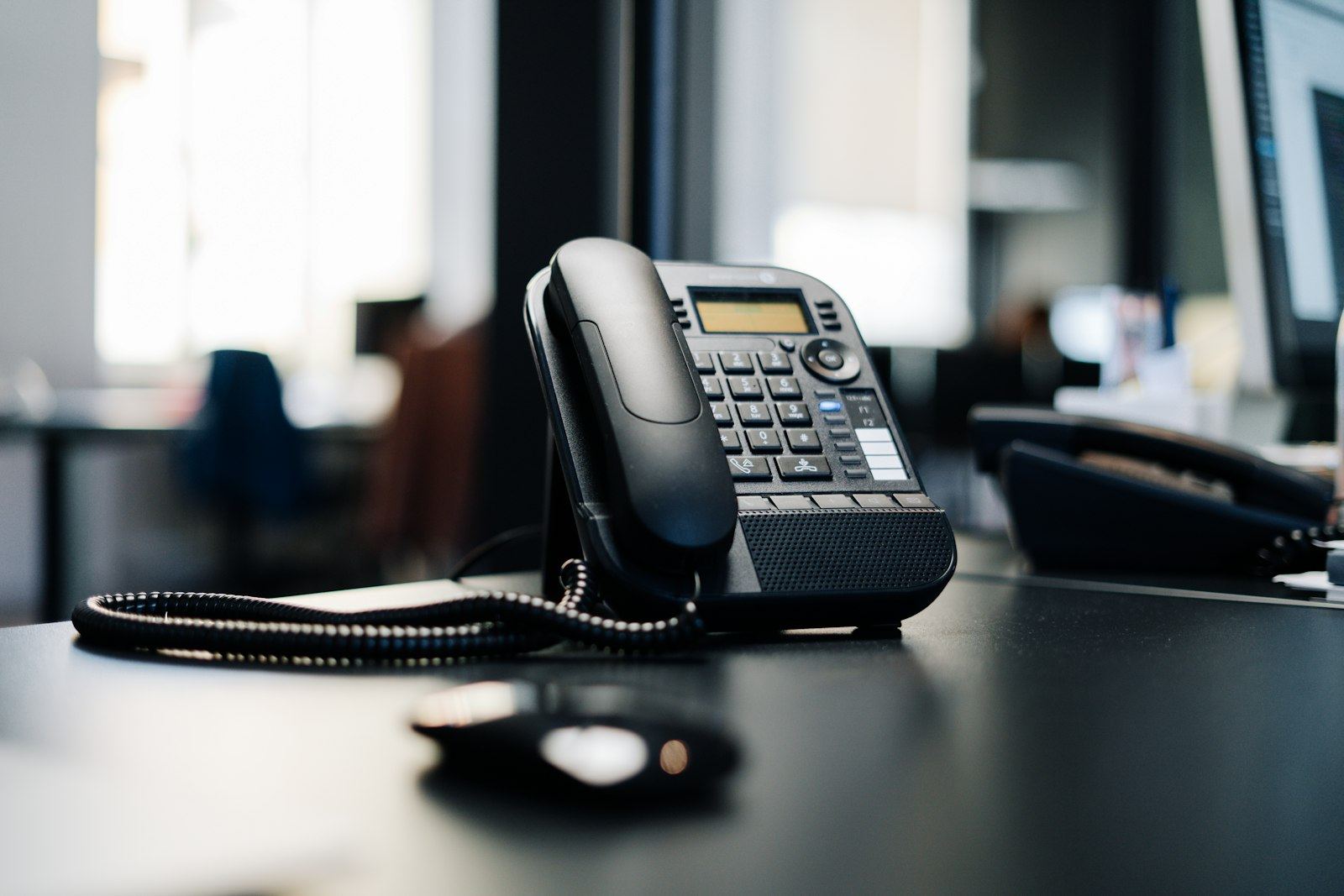 Téléphone de bureau posé sur un plan de travail, open space en arrière-plan flou